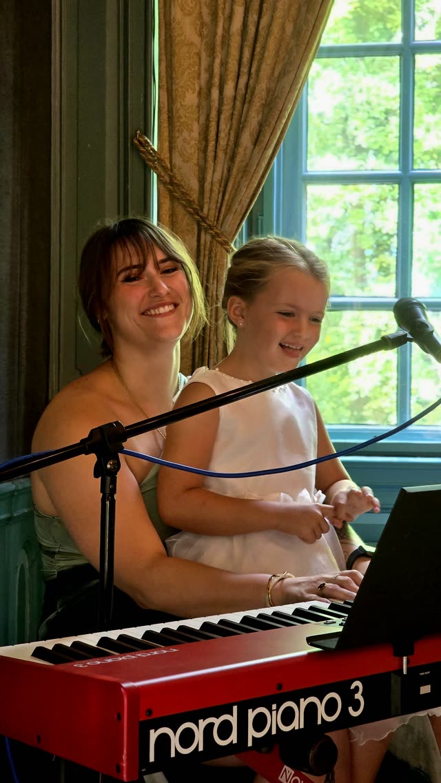 Nina samen met een bruidsmeisje bij de piano, allebei lachend