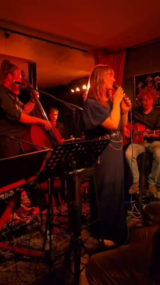 Nina zingt met haar band in een warm rood verlichte ruimte