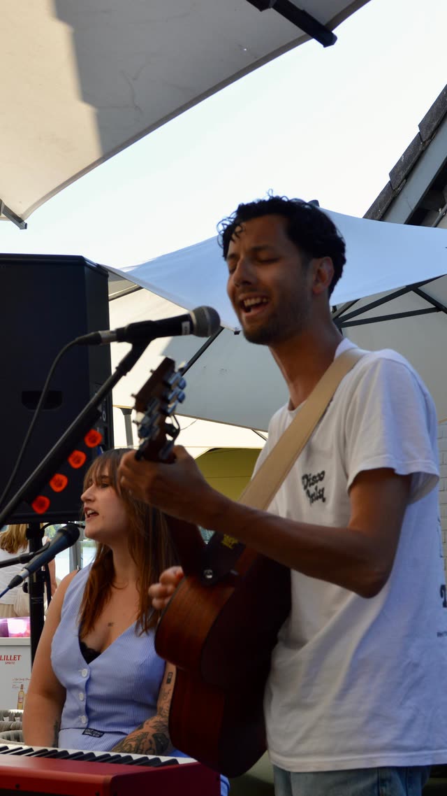 Nina zingt en speelt keyboard samen met een gitarist op een buitenoptreden bij het water