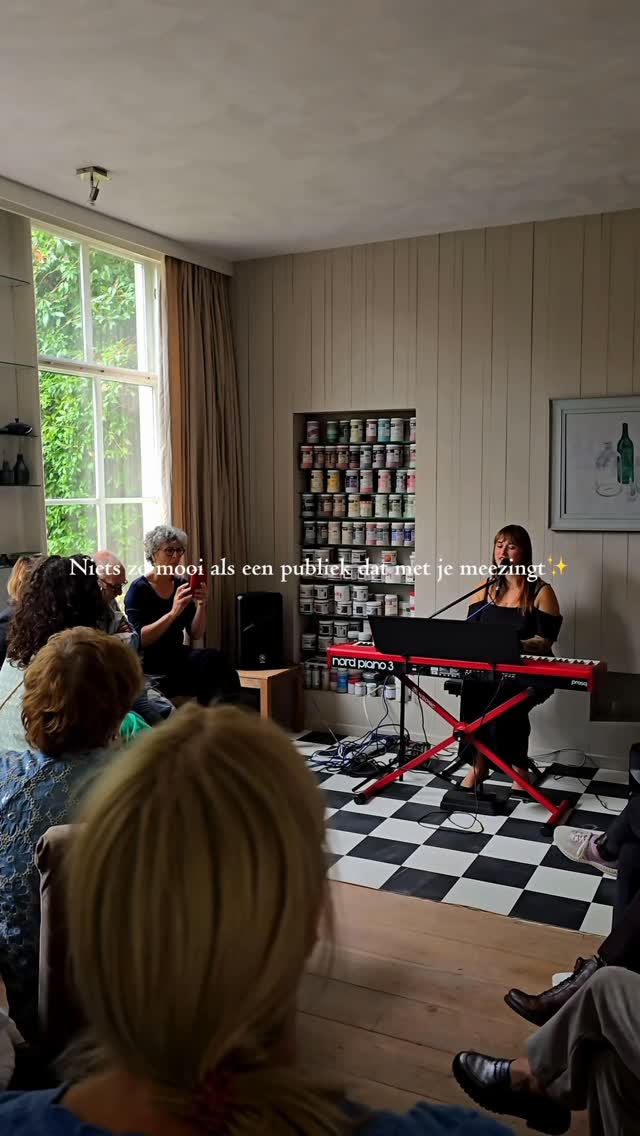 Nina speelt keyboard voor een publiek dat meezingt tijdens een huiskameroptreden