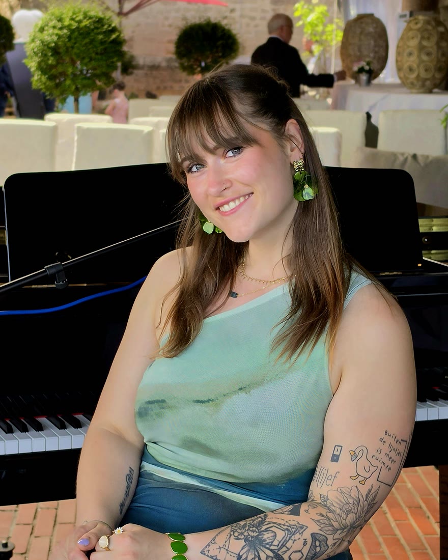 Nina lacht in de camera, zittend achter de vleugel op een terras