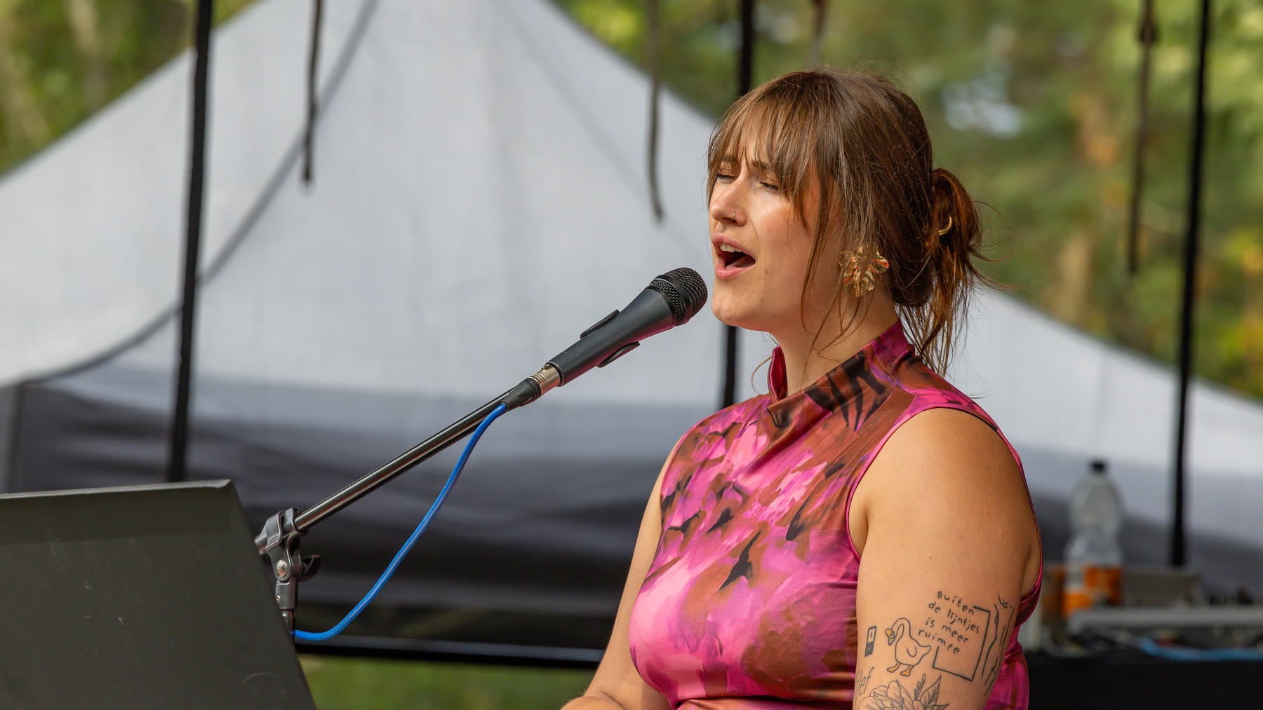 Nina Sophia zingt in een microfoon tijdens een optreden bij een tent
