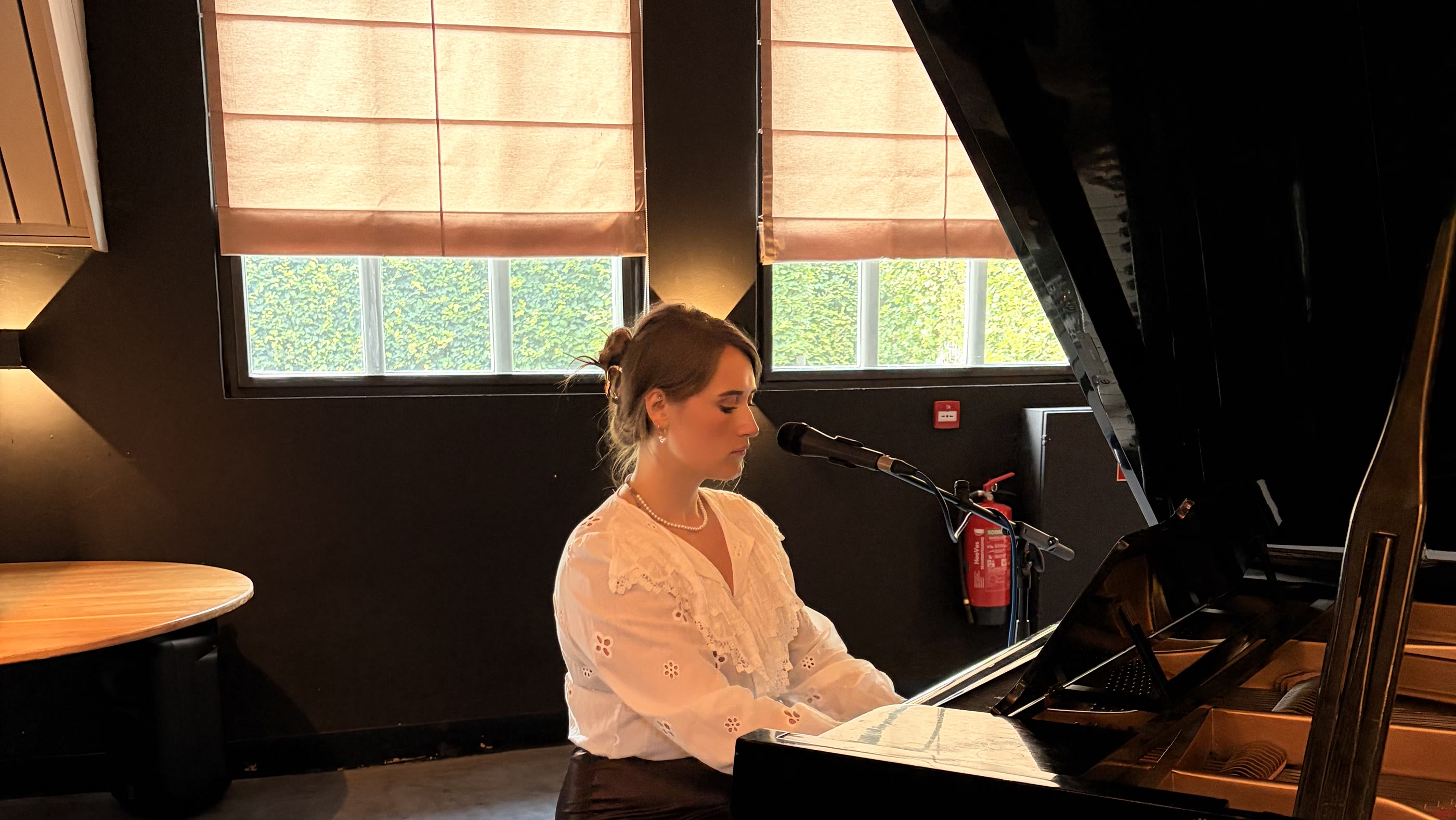 Nina Sophia zingt achter een vleugel in een lichte zaal met grote ramen