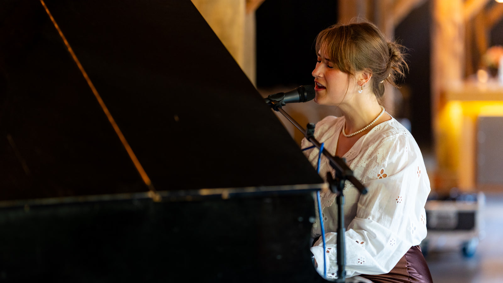 Nina Sophia zingt in de microfoon achter de vleugel, in een houten zaal met warm licht